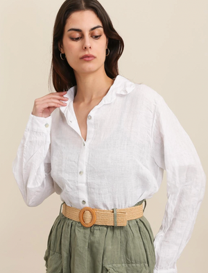 Woman wearing a white button-up shirt and green pants with a beige belt against a beige background