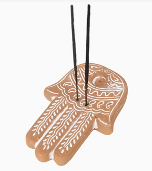 Decorative incense holder shaped like a hamsa with white patterns on a beige background
