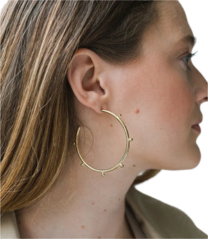 Close-up of a person wearing a gold hoop earring with a neutral background