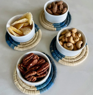 Four bowls with nuts on woven coasters on a light surface