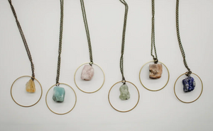 Five necklaces with circular pendants featuring different stones on a white background