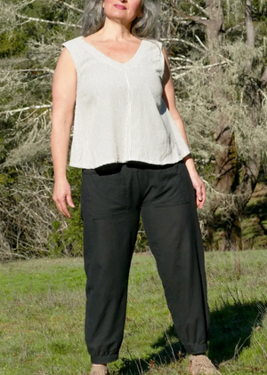 Person wearing a white sleeveless top and black pants standing in a natural setting.