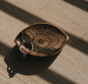 Wooden eye-shaped dish with gold earrings on a wooden surface