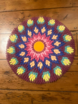 Colorful crocheted mandala mat on a wooden floor
