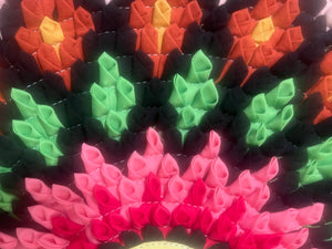Close-up of a colorful woven pattern mandala with pink, green, and orange colors.
