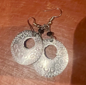Silver earrings with circular designs on a wooden surface
