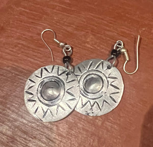 Pair of silver earrings with sunburst design on a wooden surface