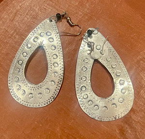 Silver teardrop earrings with intricate patterns on a brown surface