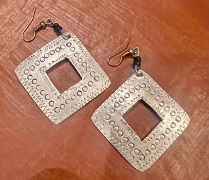 Pair of silver square earrings with textured design on a brown surface