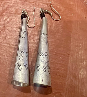 Pair of silver cone-shaped earrings with tribal patterns on a wooden surface