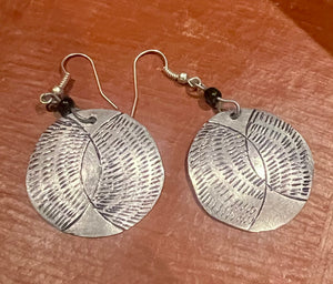 Silver earrings with leaf patterns on a wooden surface