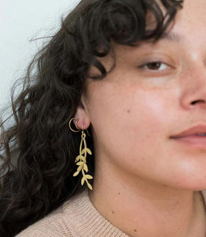 Close-up of a person wearing gold leaf earrings with a neutral background