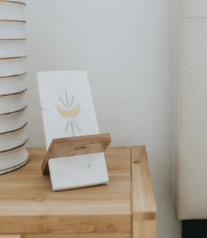 Marble and wood phone stand with gold moon design on a wooden table.