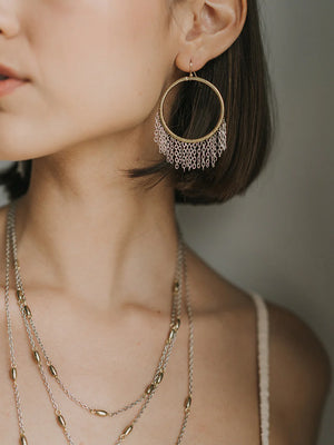 Close-up of a person wearing gold hoop earrings and necklaces against a neutral background
