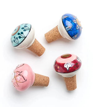 Four painted decorative mushroom-shaped bottle stoppers with cork bases on a white background