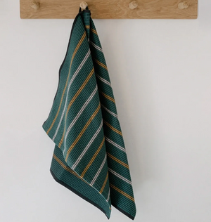 Striped green towel hanging on a wooden hook against a white wall