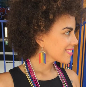 Woman wearing rainbow earrings and colorful necklaces with a blurred background