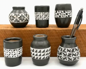 Set of black ceramic vases with geometric patterns on a wooden shelf.