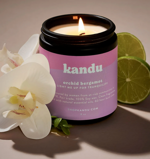 Kandu candle with orchid and bergamot scents, surrounded by flowers and limes on a neutral background