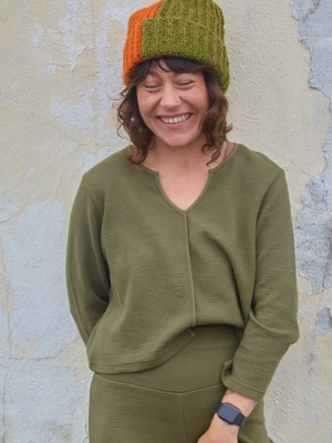 Person wearing a green knit hat and matching outfit against a textured wall.