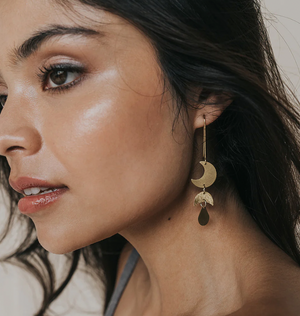 Close-up of a woman wearing gold earrings with a moon phase design