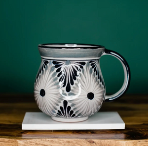 Ceramic mug with black and white pattern on a wooden surface and green background