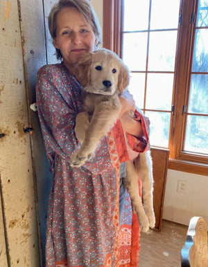 Woman wearing a duster robe with floral pattern holding a puppy indoors near a window