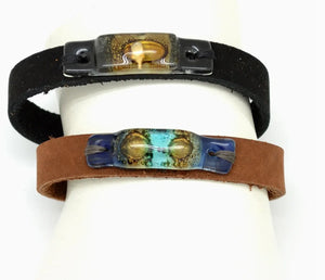 Two leather bracelets with decorative metal plates on a white background