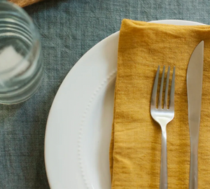 White plate with a yellow fabric napkin, fork, and knife on a textured surface.