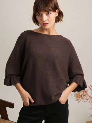 Woman wearing a brown dolman sweater against a neutral background