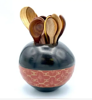 Black ceramic holder with floral patterns containing wooden spoons on a white background