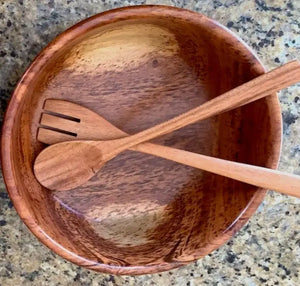 Wooden salad bowl with two wooden utensils on a speckled countertop
