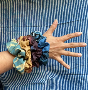 Hand wearing a colorful scrunchie with a striped fabric background