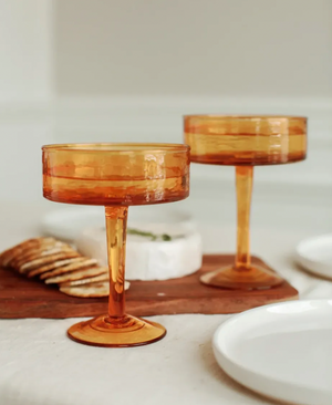 Two amber-colored cocktail glasses on a table with a blurred background