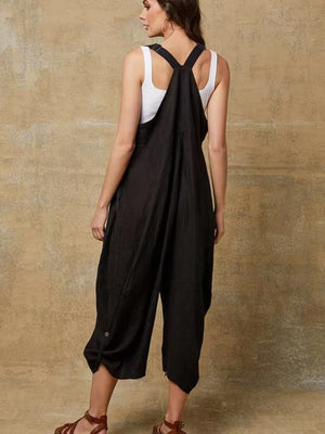 Woman wearing a black overalls and white top against a beige wall