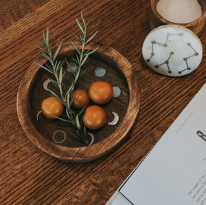 Round wooden tray with orange spherical objects and herbs on a wooden surface with a book.