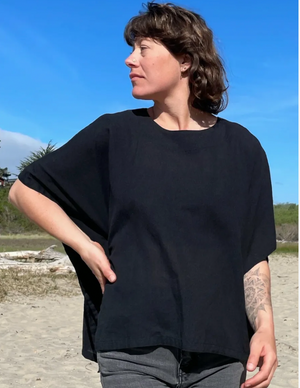 Person wearing a black boxy top on a beach with a clear blue sky.