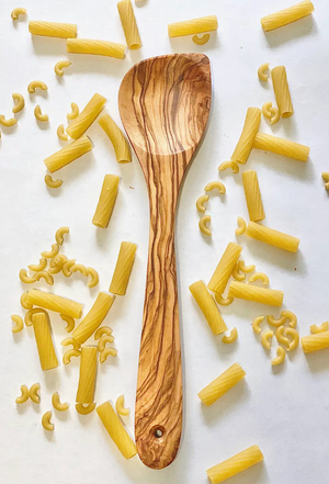 Wooden spoon on a white surface with scattered pasta