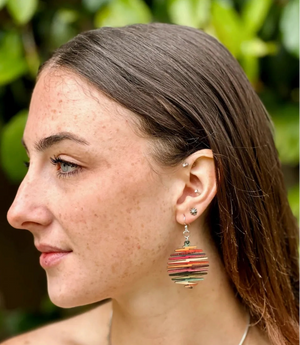 Close-up of a woman wearing colorful earrings with a blurred green background