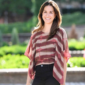 Woman wearing a red and beige striped top outdoors with greenery in the background