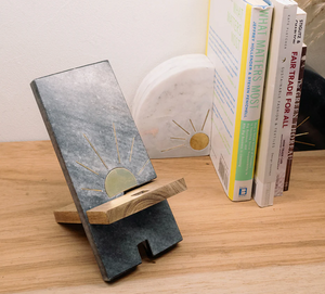 Phone stand with sun design on a wooden surface with books in the background