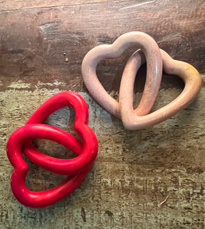 Two heart-shaped objects, one red and one beige, on a wooden surface.