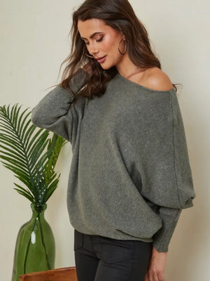 Woman wearing a gray off-shoulder sweater with a plant in the background