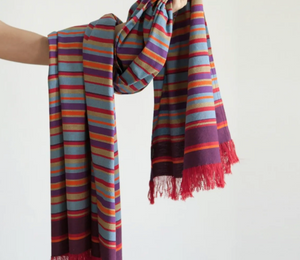 Multicolored striped scarf with fringes held by a person against a white background