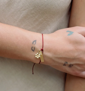 Close-up of a wrist wearing a gold bracelet with a small charm, against a neutral background.