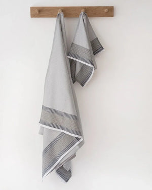 Two gray towels with decorative patterns hanging on a wooden rack against a white wall.