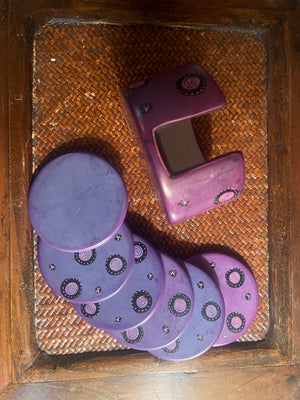 Set of purple coasters and holder with a decorative pattern on a woven surface
