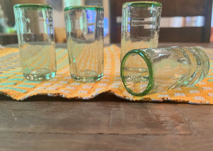 Four clear shot glasses with green rims on a patterned cloth