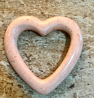 Heart-shaped object with a pinkish hue on a textured surface