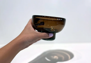 Hand holding a dark brown glass against a white background